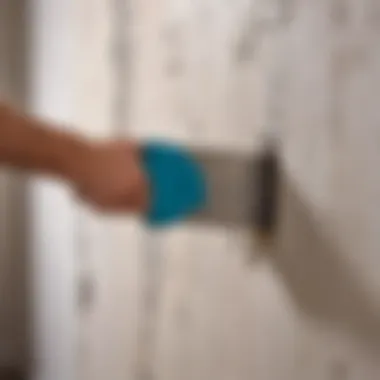 Close-up of a wall scraper being used on a wallpapered surface